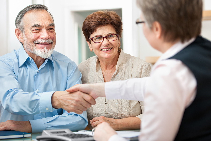 senior couple smiling while shaking hand with financial advisor